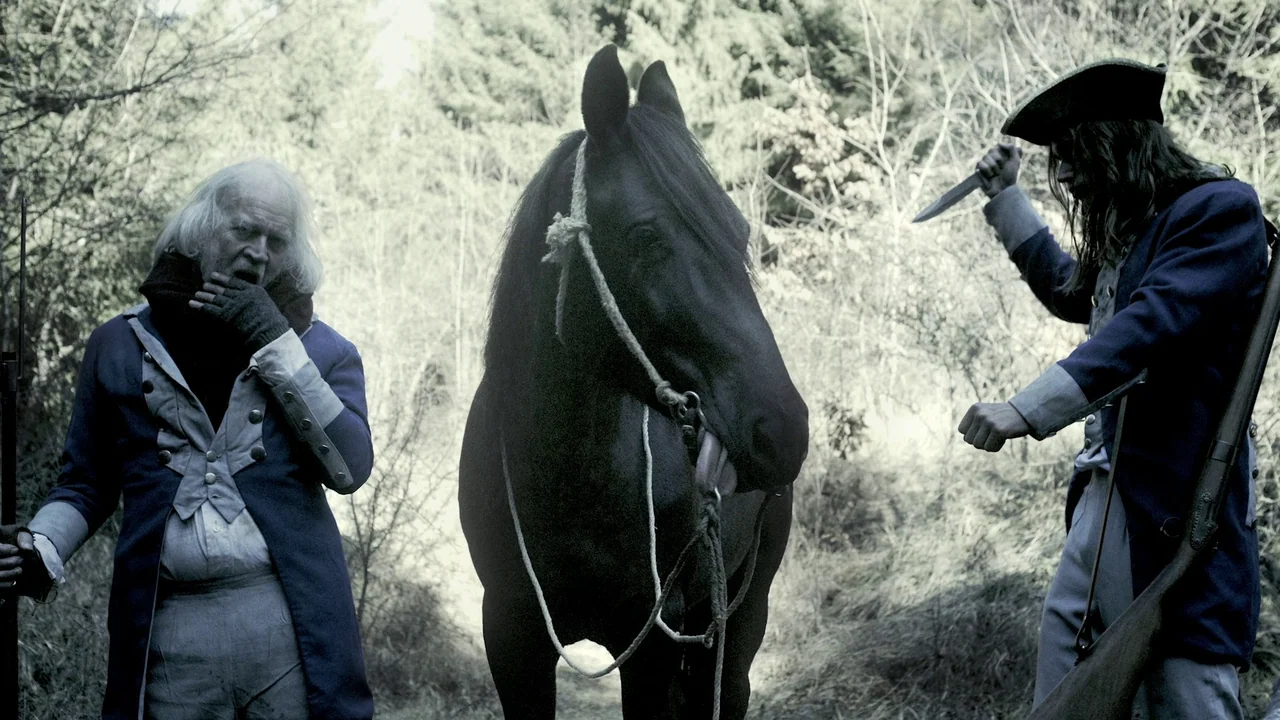 Helll Hole (2024) movie still: medium — A desolate woodland clearing with dense trees and sparse undergrowth in autumn. An elderly man stands…