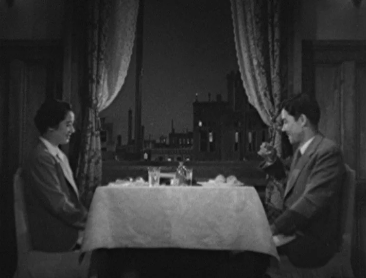 No Regrets for Our Youth (1946) movie still: medium — A man and a woman sit at a table in a room with a window. Outside the window, a dark cityscape…