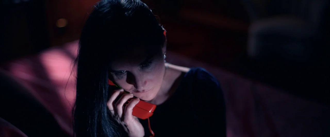 The Substance (2024) movie still: closeup — A dark bedroom interior features a woman bathed in low-key lighting. She sits on a surface while holding…