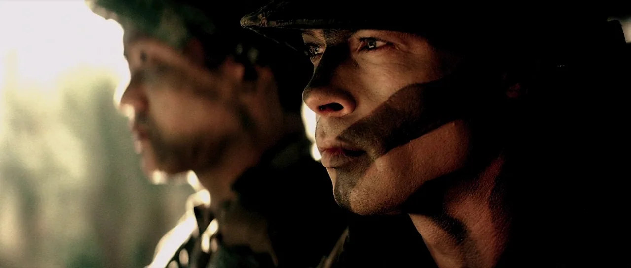 Spy Game (2001) movie still: medium — Two soldiers in combat gear sit together inside a moving vehicle. Bright sunlight streams from the rear,…