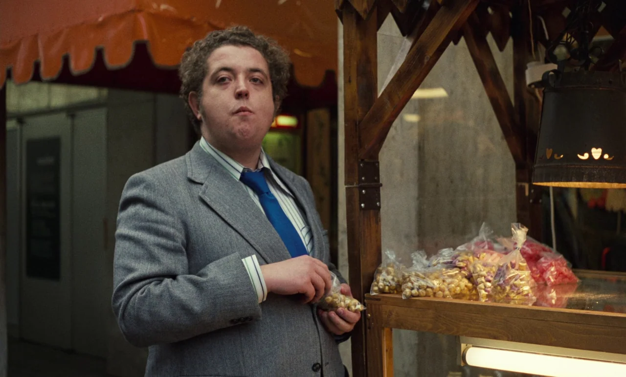 Wrong Move (1975) movie still: medium — A man stands next to a wooden vendor stand filled with small bags of candy. He holds a clear plastic bag…