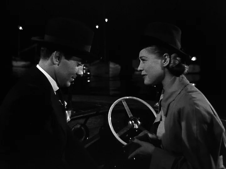 Nightmare Alley (1947) movie still: medium — Two people in hats face each other at night near a car steering wheel. The background features dark…
