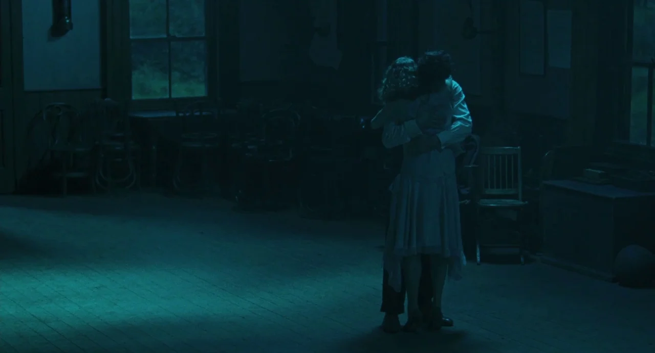 Jimmy’s Hall (2014) movie still: fullbody — A dimly lit, empty wooden hall contains stacked chairs and two large windows. A man and a woman in…