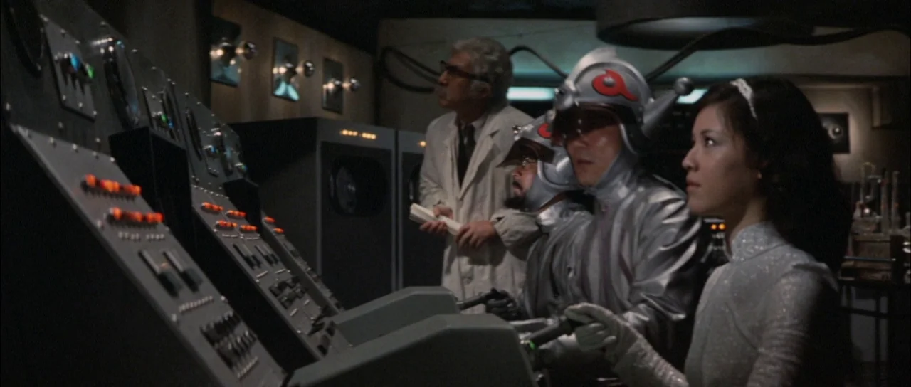 Terror of Mechagodzilla (1975) movie still: medium — A dimly lit industrial room features a large control panel with glowing switches and buttons.…