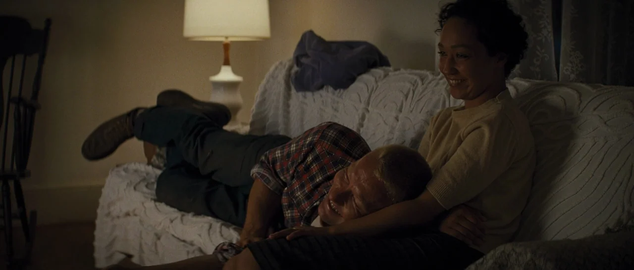 Loving (2016) movie still: medium — A dimly lit room features a couch covered with a white textured throw blanket. A man rests his head on a woman's…