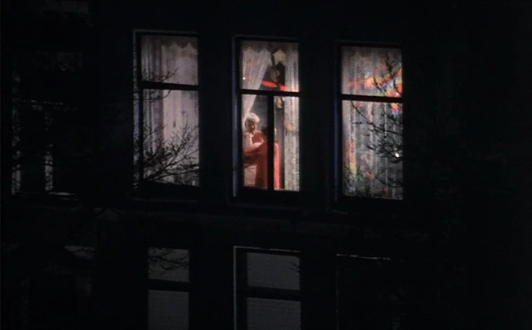 Business is Business (1971) movie still: wide — The exterior facade of a multistory building is shrouded in total night darkness. A single window on…