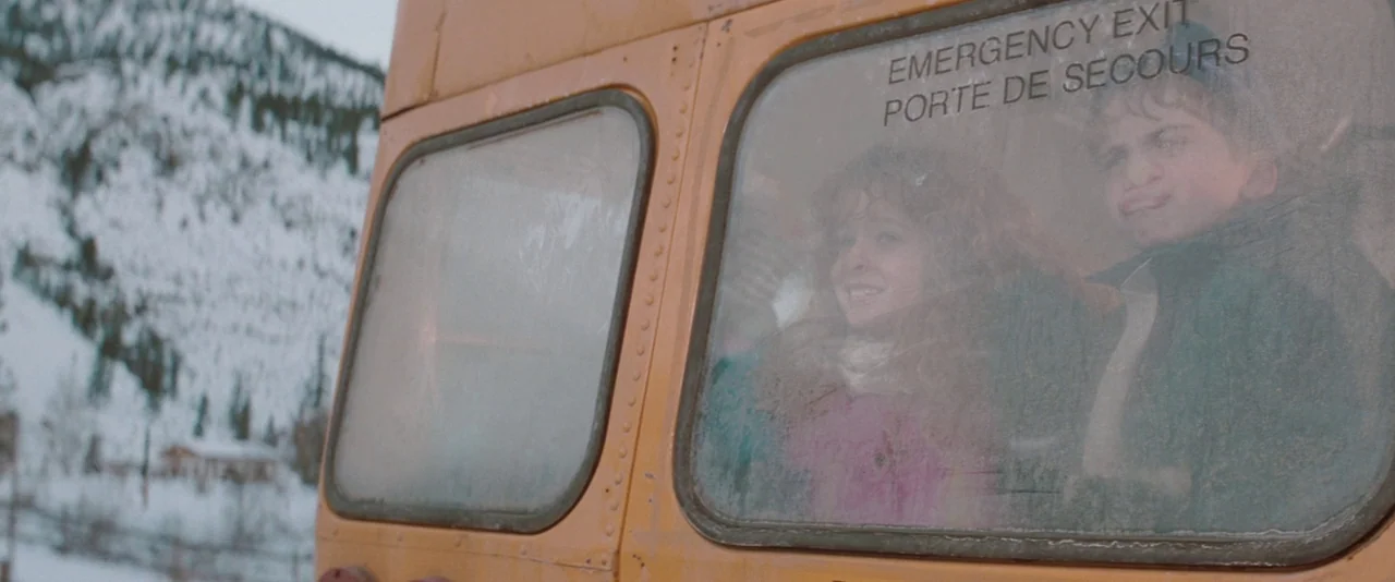 The Sweet Hereafter (1997) movie still: medium — A yellow school bus is parked in a snowy mountainous landscape. Two children look out through the…