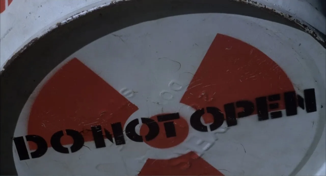 Empire of the Ants (1977) movie still: closeup — A close-up view of a circular white metal container lid with a radiation symbol. The words DO NOT…