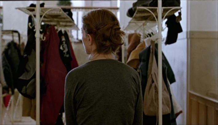 The Piano Teacher (2001) movie still: A woman stands motionless in the narrow corridor of a cloakroom, surrounded by a dense array of hanging coats.…