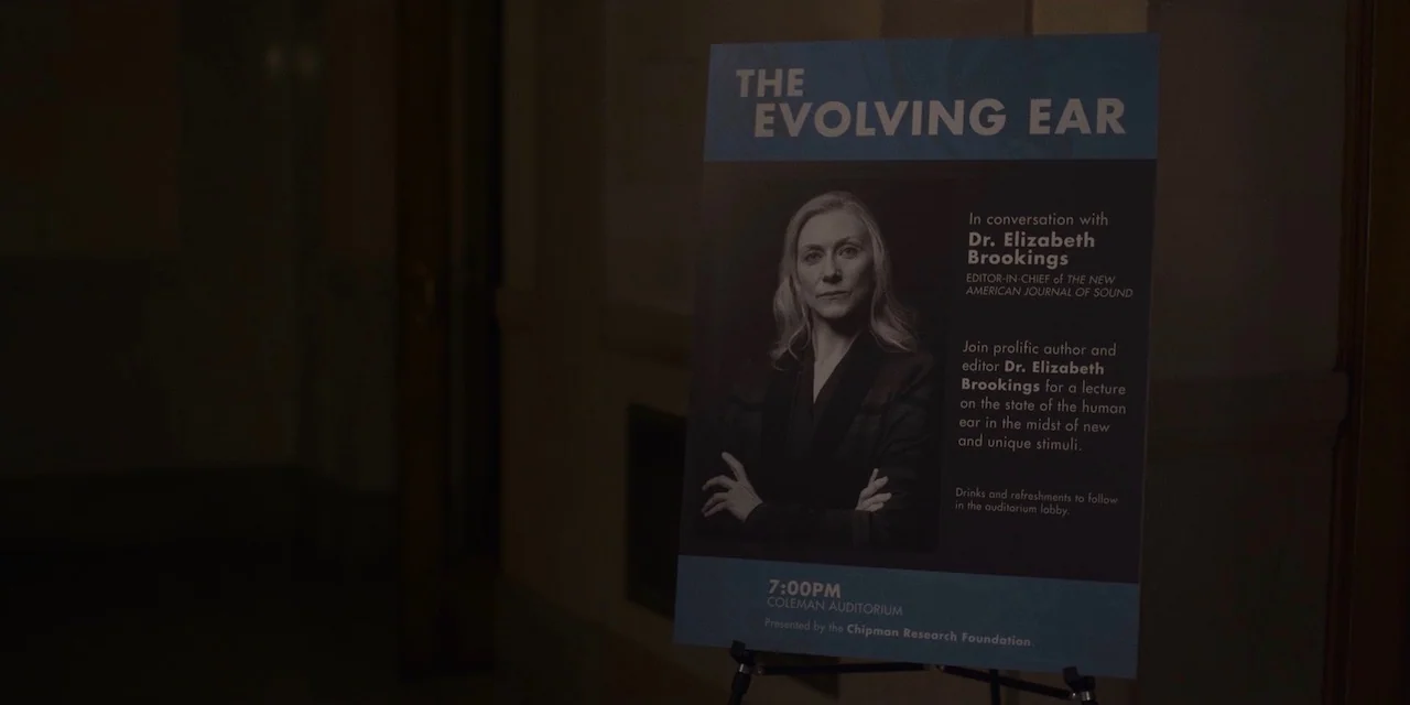 The Sound of Silence movie still: closeup — An informational sign stands in a darkened hallway of a public building. The poster displays details for…