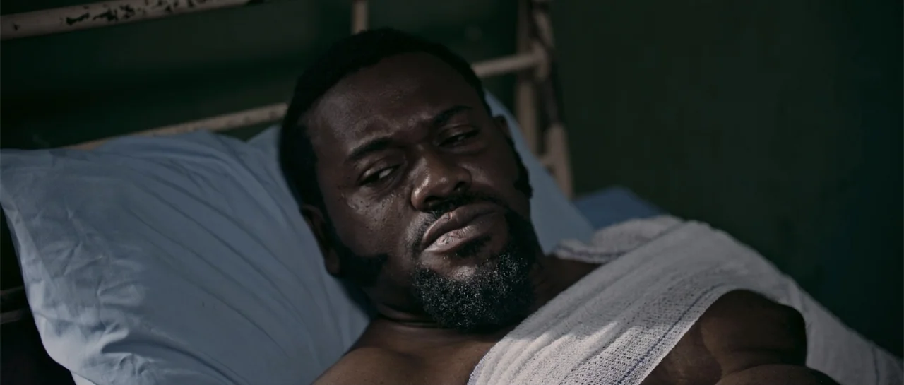 Crossroads (1986) movie still: closeup — A dark hospital room contains a metal-framed bed with a light blue pillow. A man with a bandaged torso lies…