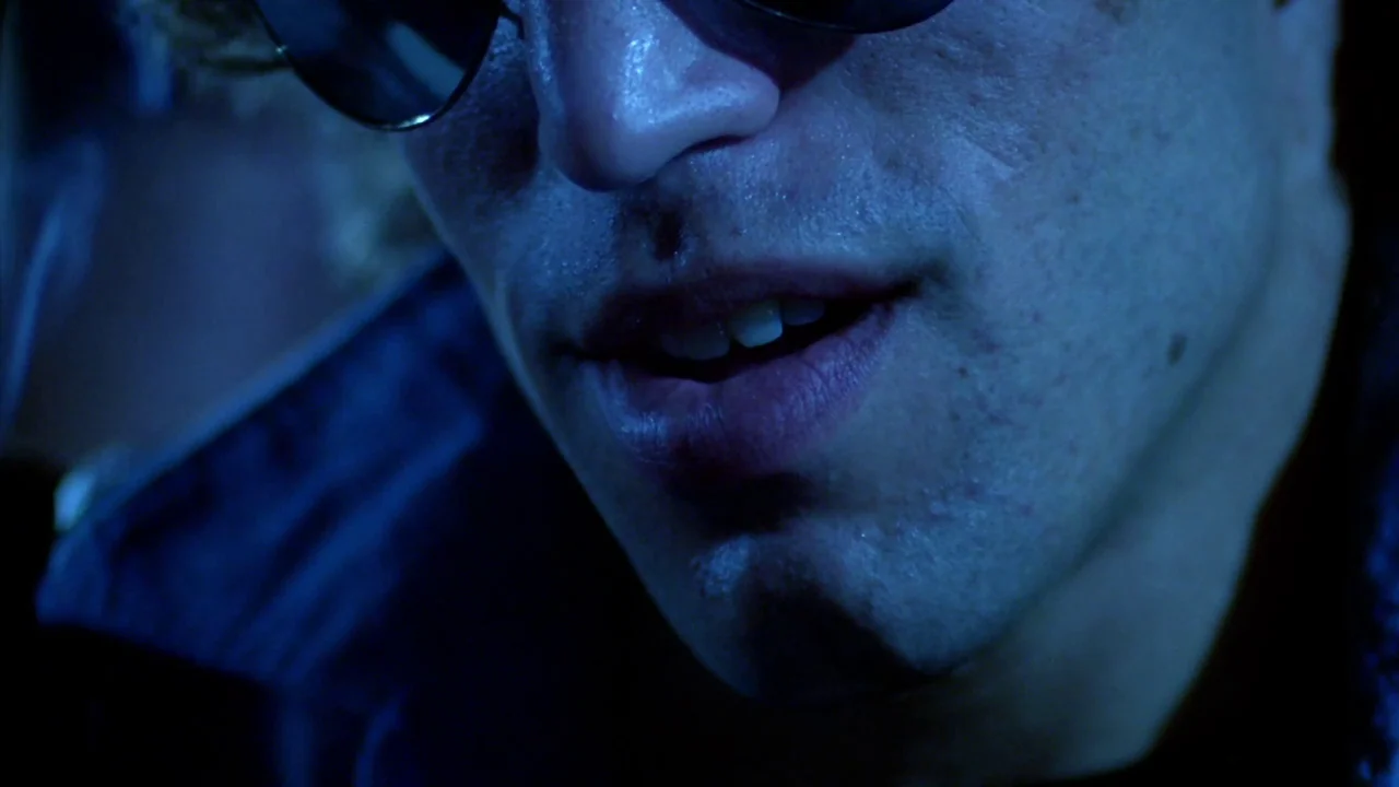Cruising (1980) movie still: closeup — A dimly lit club interior glows with intense blue light against the subject. The subject's lower face is…