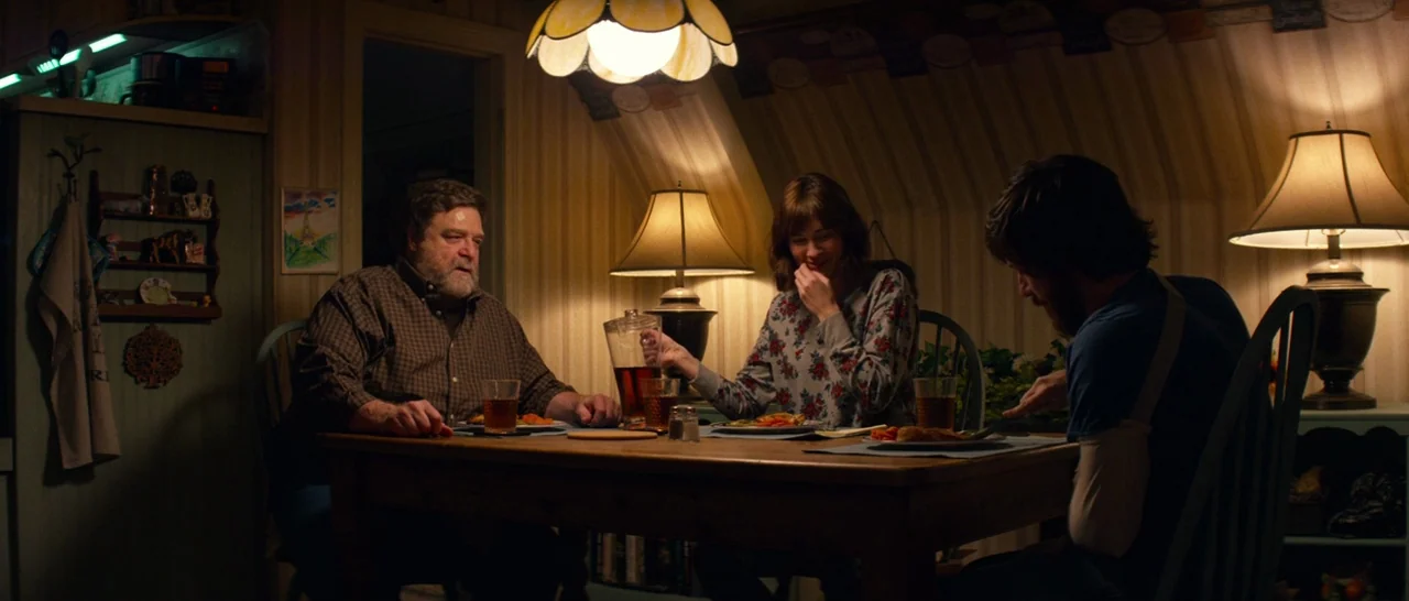 10 Cloverfield Lane (2016) movie still: medium — A dimly lit dining area featuring striped wallpaper and a wooden table. Three people are seated…