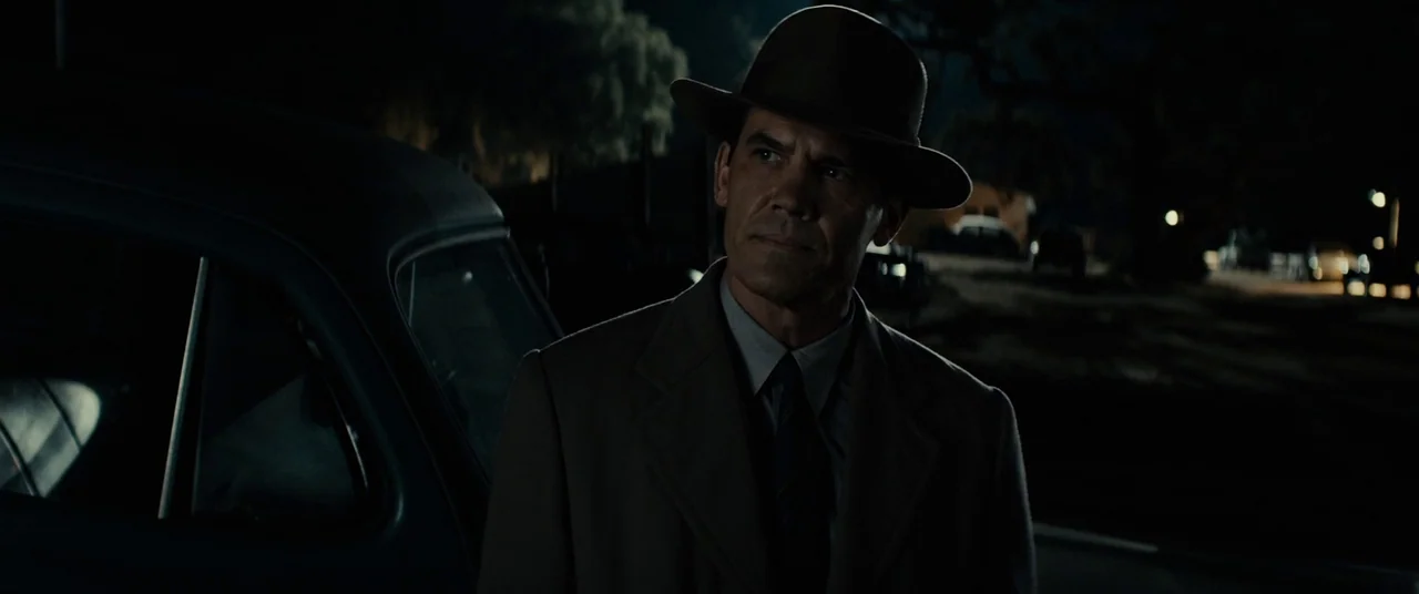 Gangster Squad (2013) movie still: medium — A dark night setting features a man standing beside the dark silhouette of a car. He gazes off-screen in…