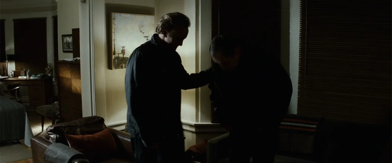 Hereafter (2010) movie still: medium — A dimly lit room with walls painted in light tones and a piece of framed artwork. Two men stand close…