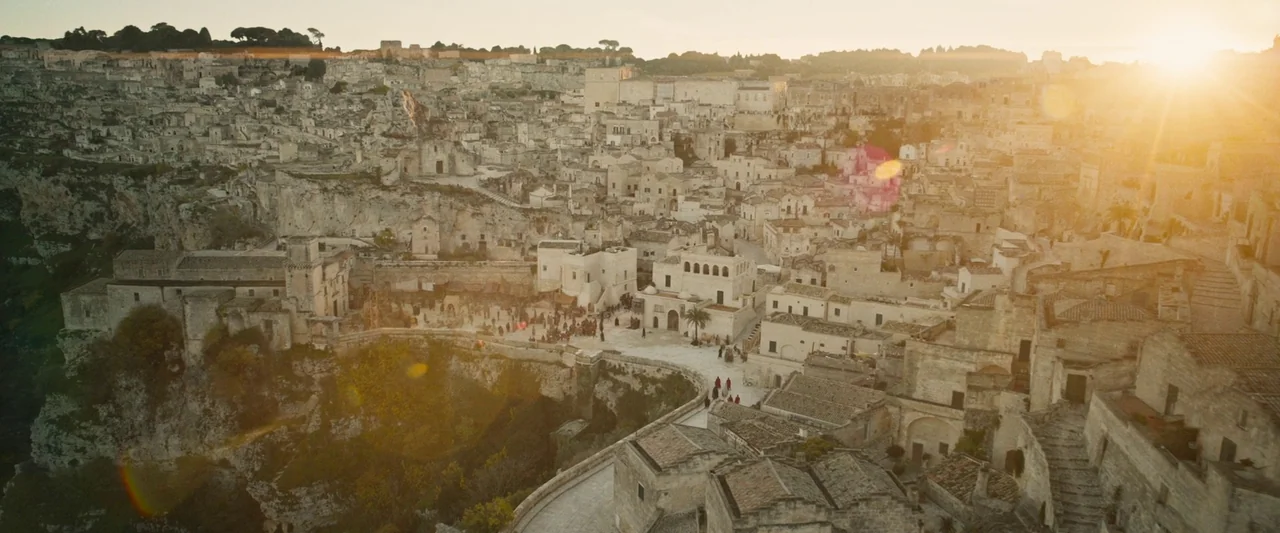 The Book of Clarence (2023) movie still: establishing — An ancient stone city carved into a rocky cliffside with densely packed buildings. People…