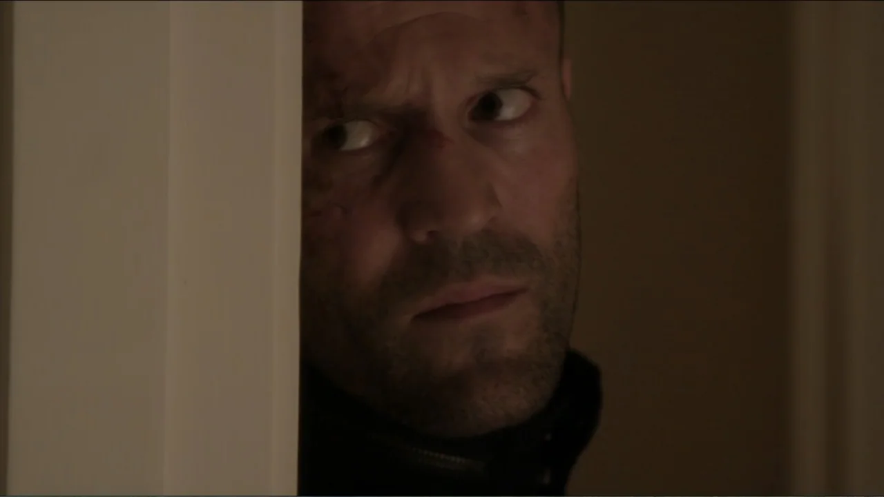 Parker (2013) movie still: closeup — An interior space features a dark doorway partially obscuring a man's face. The man peers around the vertical…