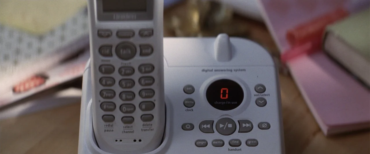 He's Just Not That Into You (2009) movie still: closeup — A digital cordless telephone sits on a wooden surface with papers in the background. The…