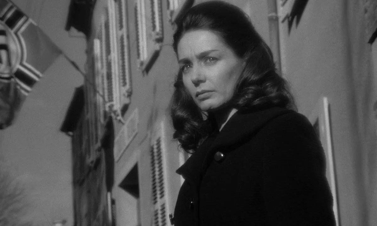 Léon Morin, Priest (1961) movie still: medium — A European street features a building with shuttered windows and a prominent hanging flag. A woman…