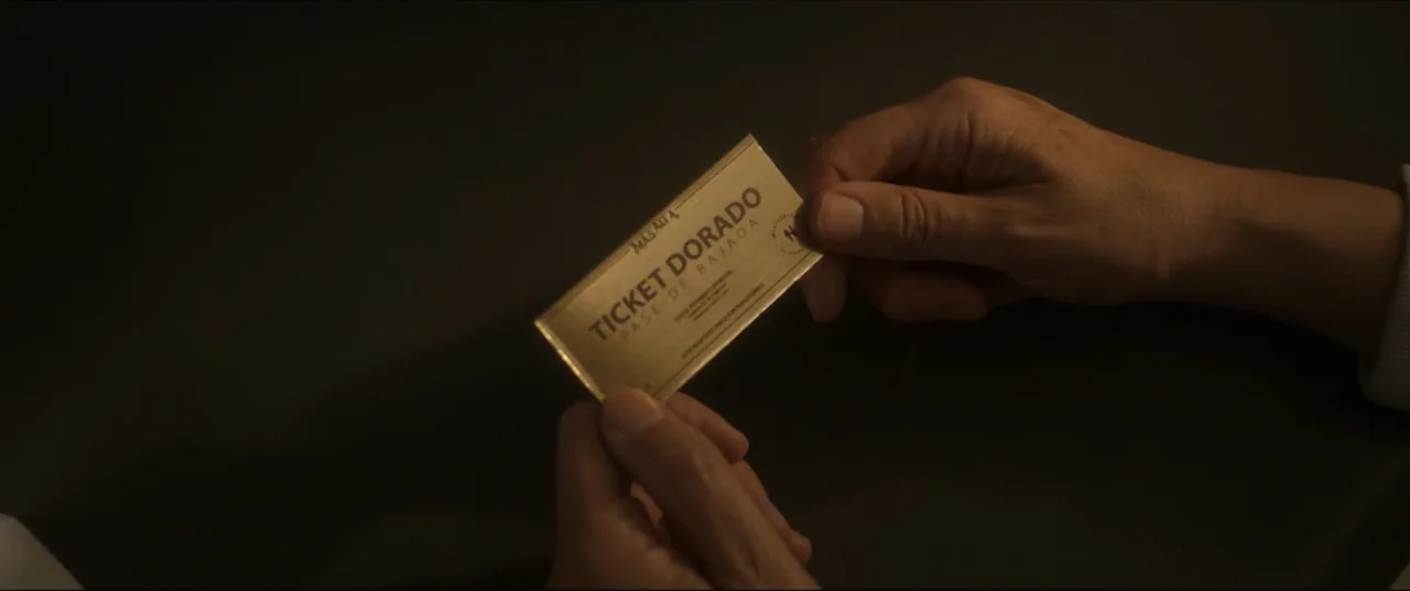 Can't Quit Mom (2022) movie still: closeup — A golden rectangular ticket is held by two hands against a dark, featureless backdrop. The hands are…