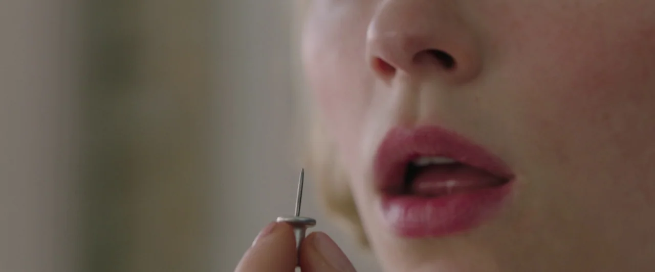 Swallow (2020) movie still: closeup — A close-up view shows a person's lower face and nose in a brightly lit room. The person holds a metal thumb…