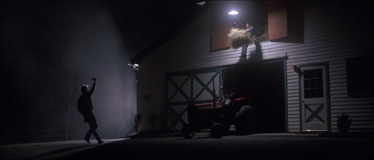 At Close Range (1986) movie still: wide — A white wooden structure at night features a glowing light above an open loft. A person tosses a bundle of…