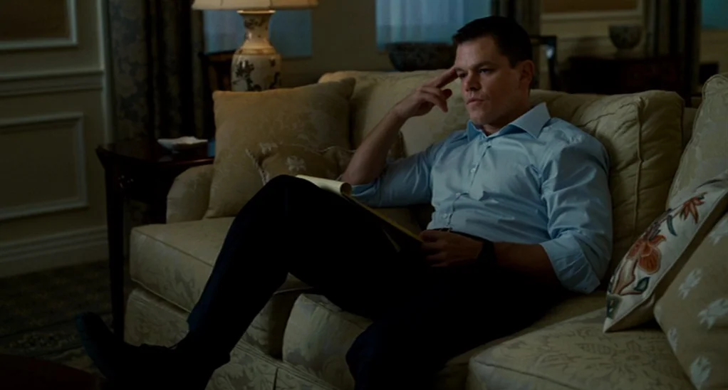 The Adjustment Bureau (2013) movie still: medium — A hotel suite features upholstered furniture, a table lamp, and classic wall paneling details. A…