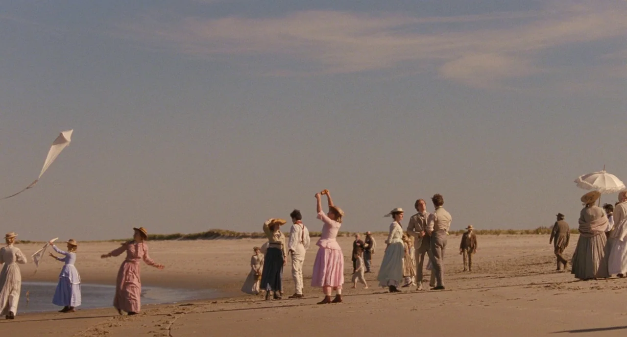 Little Women (2019) movie still: wide — A group of people in 19th-century period clothing gather on a wide, sandy beach. Several individuals fly a…