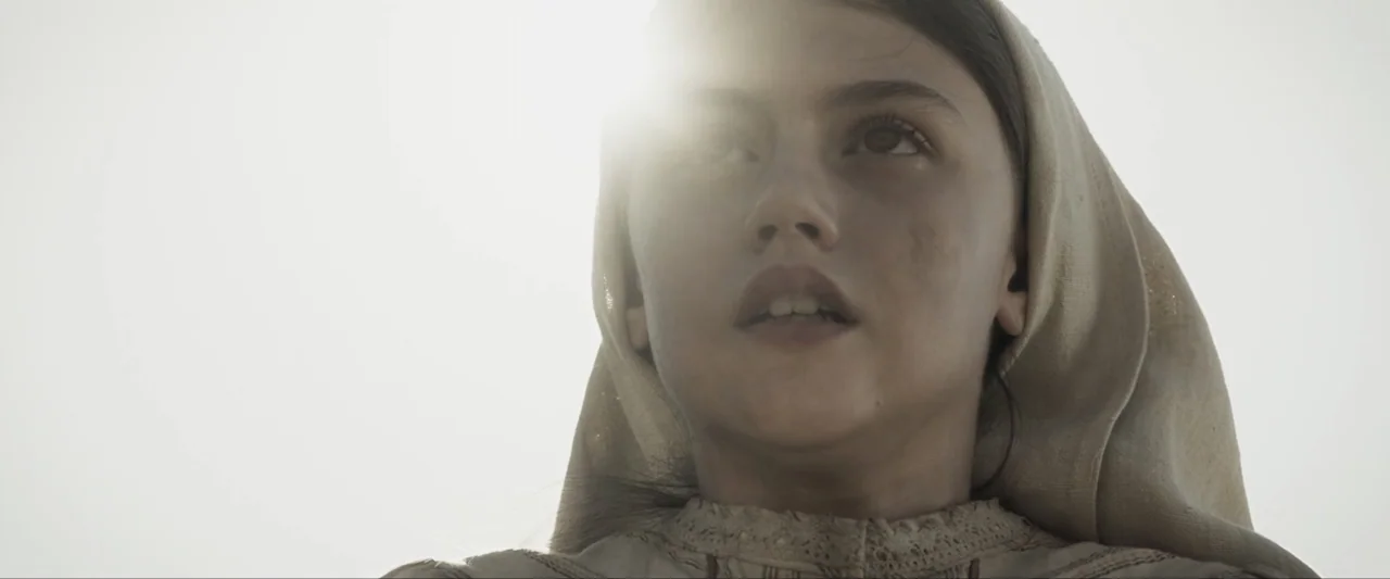Fatima (2020) movie still: closeup — A person stands in a bright outdoor environment under harsh sunlight. The subject looks toward the sky with a…