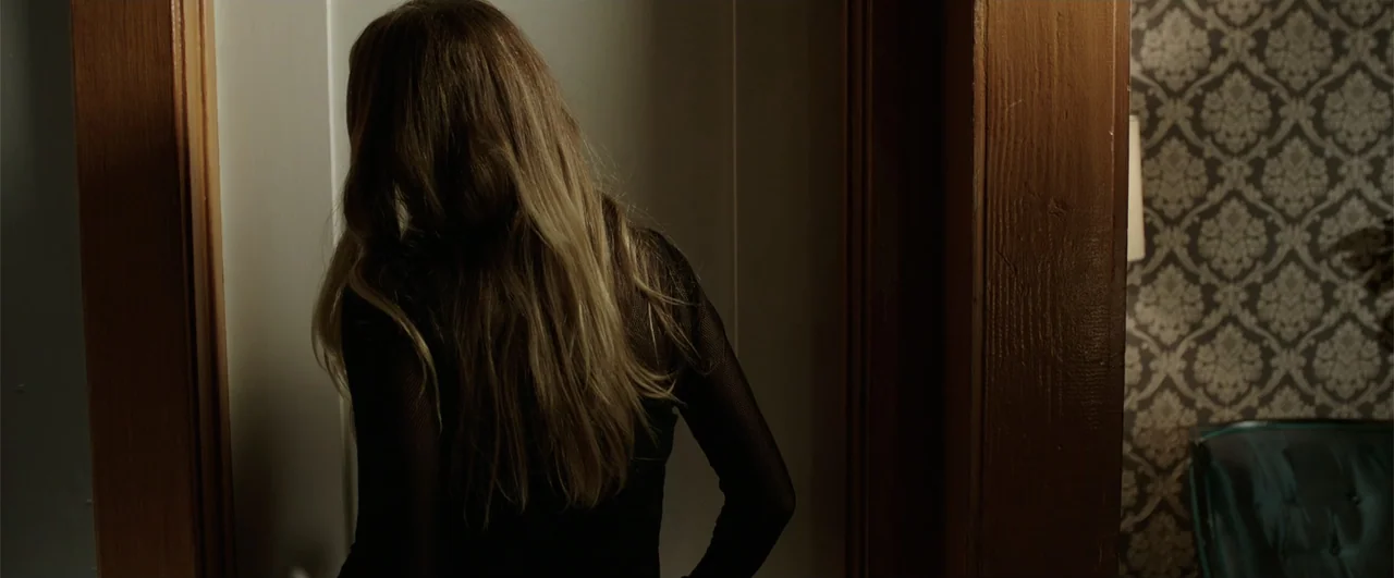 Lights Out (2016) movie still: medium — A dark indoor doorway frames a woman standing with her back to the camera. The adjacent wall features…