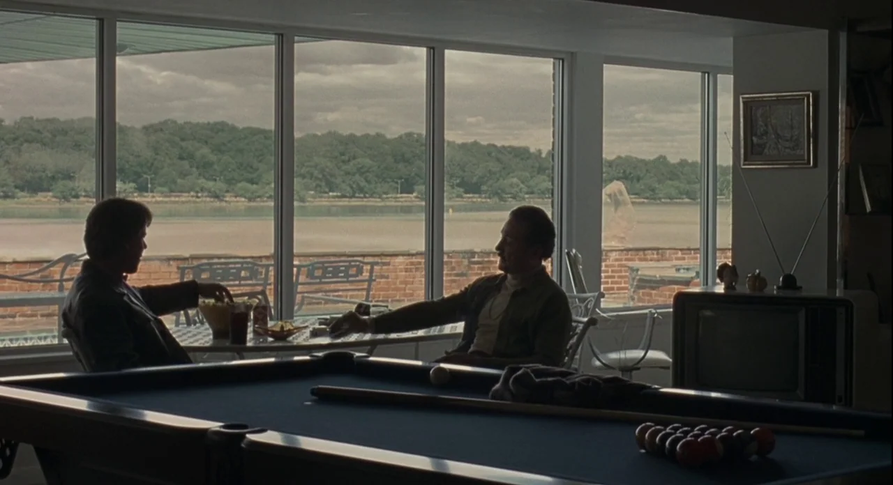 American Gangster (2007) movie still: wide — A game room with a pool table features large windows overlooking a waterfront area. Two men sit at a…
