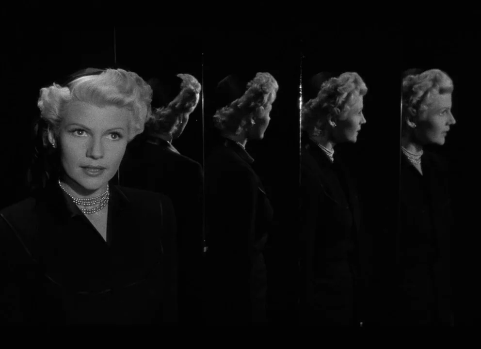 The Lady from Shanghai (1947) movie still: closeup — A woman stands in a dark space featuring multiple vertical mirror reflections of herself. She…