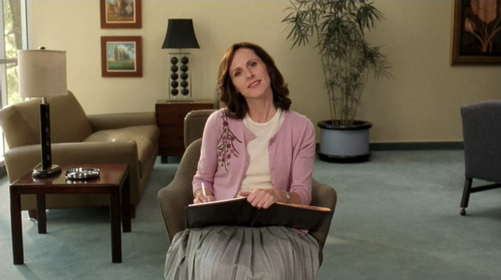 Year Of The Dog (2007) movie still: medium — A quiet professional reception or waiting area features beige walls and green carpeting. A woman sits…