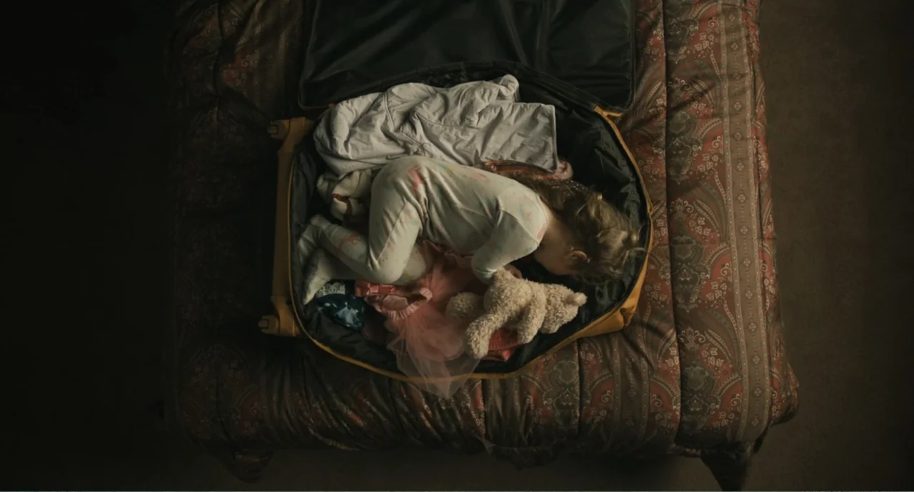Bad Boys: A True Story (2003) movie still: medium — A patterned bedspread holds a large yellow suitcase containing a sleeping child and clothes. A…