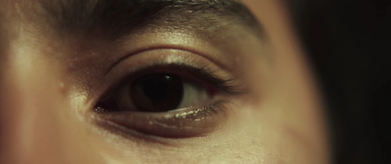 Sea Fever (2019) movie still: closeup — An extreme close-up focuses on a human eye and surrounding skin detail. The eye remains still under low-key…