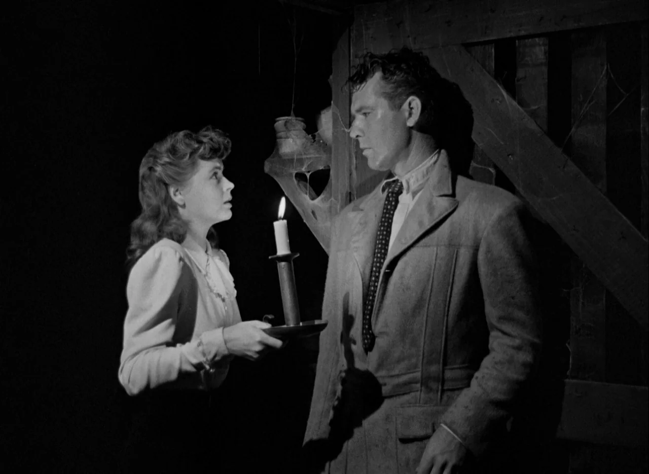 The Spiral Staircase (1946) movie still: medium — A dimly lit wooden barn interior with visible spiderwebs hanging on a structural frame. A woman…
