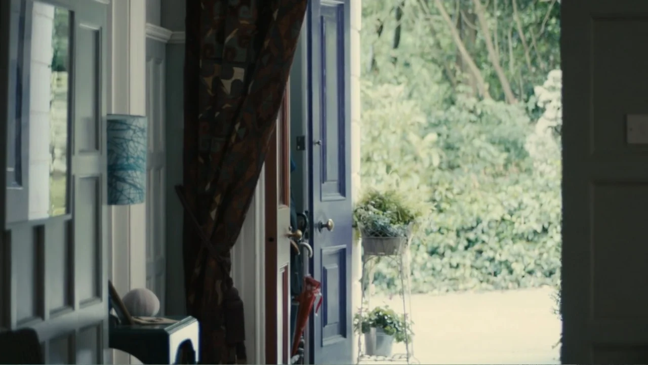 About Time (2013) movie still: medium — An interior entryway shows a partially open dark blue door leading to a garden. A small metal plant stand…