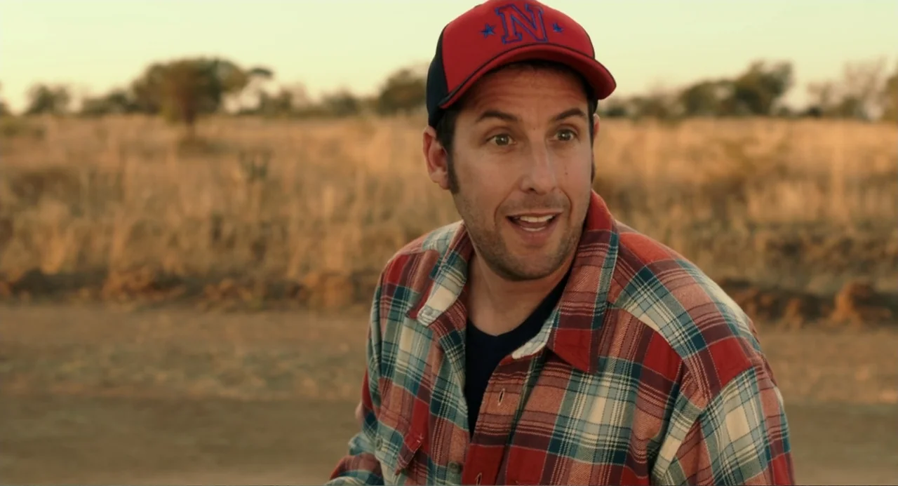 Blended (2014) movie still: medium — A man stands in a dry, grassy savanna under golden hour light. He is speaking while turned three-quarters away…