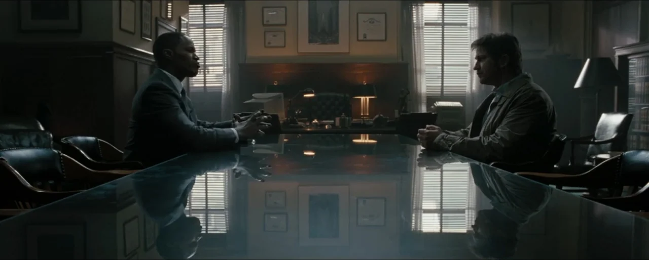 Law Abiding Citizen (2009) movie still: medium — A dark wood-paneled room features a large reflective glass table and shuttered windows. Two men sit…