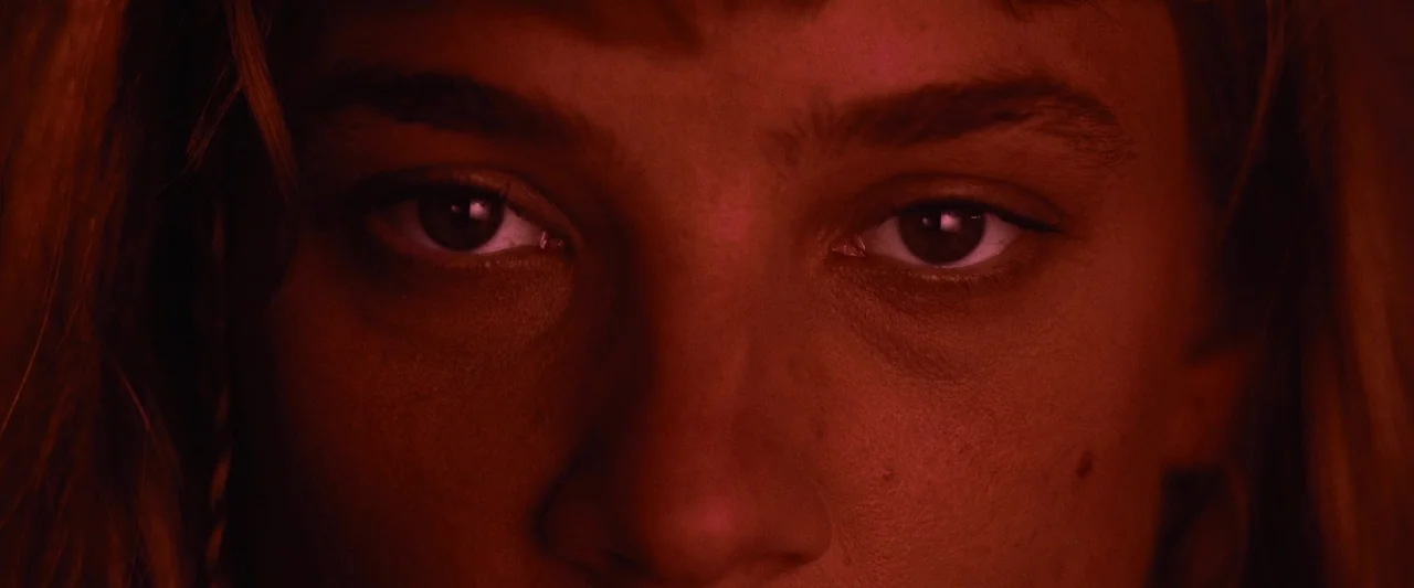 Meanwhile On Earth (2024) movie still: closeup — A close-up view shows a woman's eyes and nose in a dark environment. The entire frame is cast in…