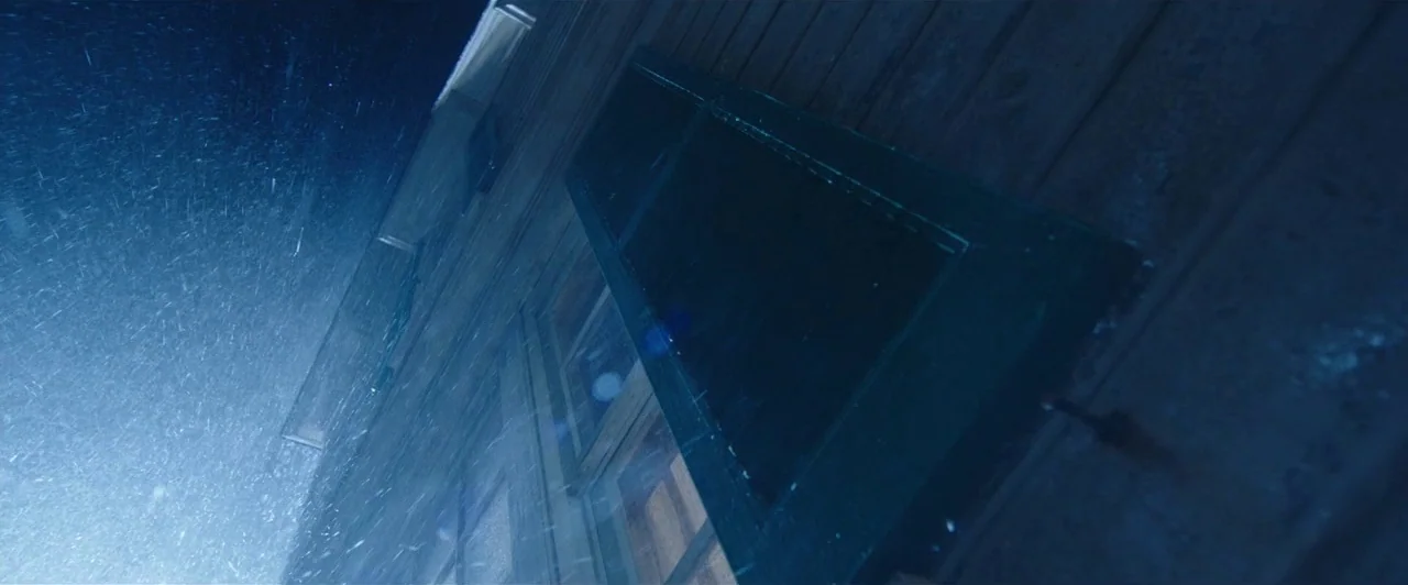 Aquaman (2018) movie still: establishing — The exterior wall of a dark wooden house is battered by heavy nighttime snow. A single closed dark…