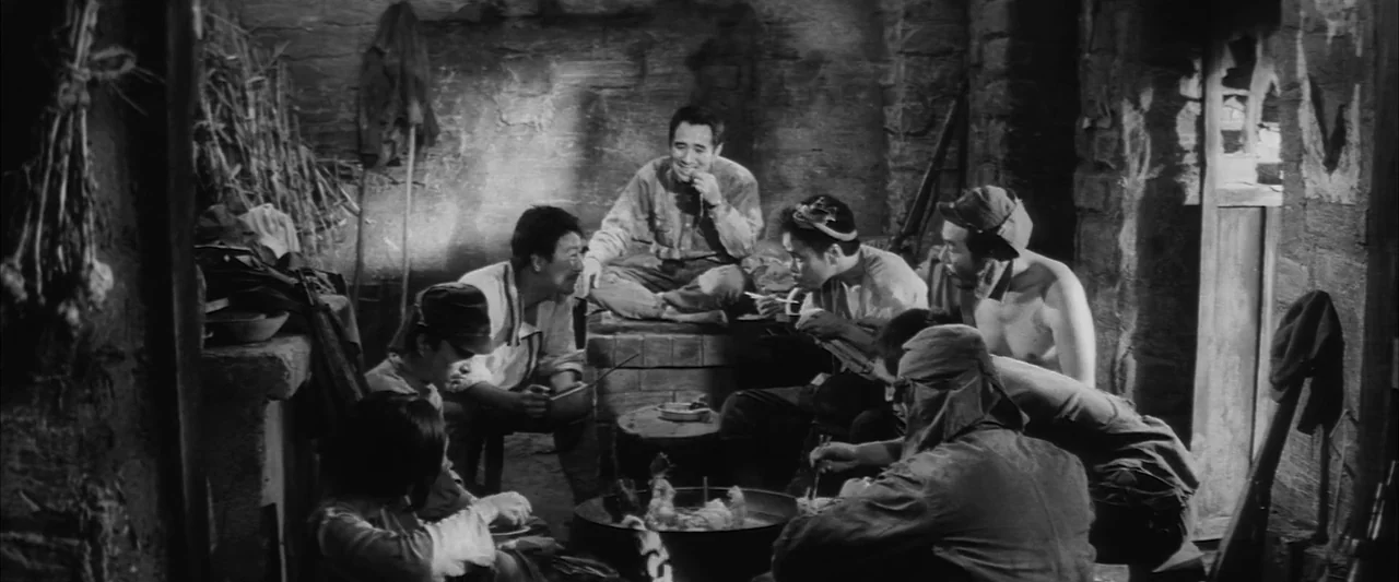 The Human Condition III: A Soldier’s Prayer (1961) movie still: medium — A rustic stone-walled hut features a central cooking pot surrounded by…