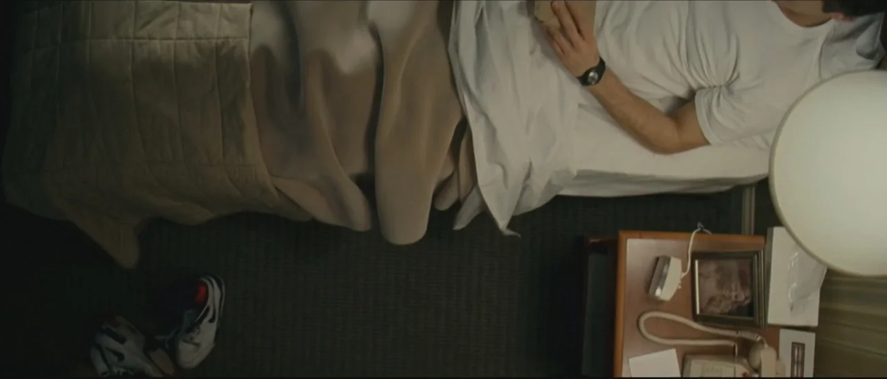 Definitely, Maybe (2008) movie still: medium — A top-down view of a person lying in a bed within a hotel room. The subject wears a white t-shirt and…