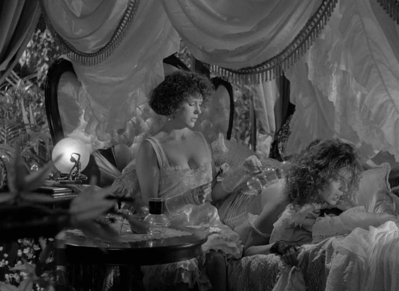 Singapore Sling (1990) movie still: medium — A dark bedroom features a canopy bed adorned with thick, gathered white fabric curtains. A woman in a…