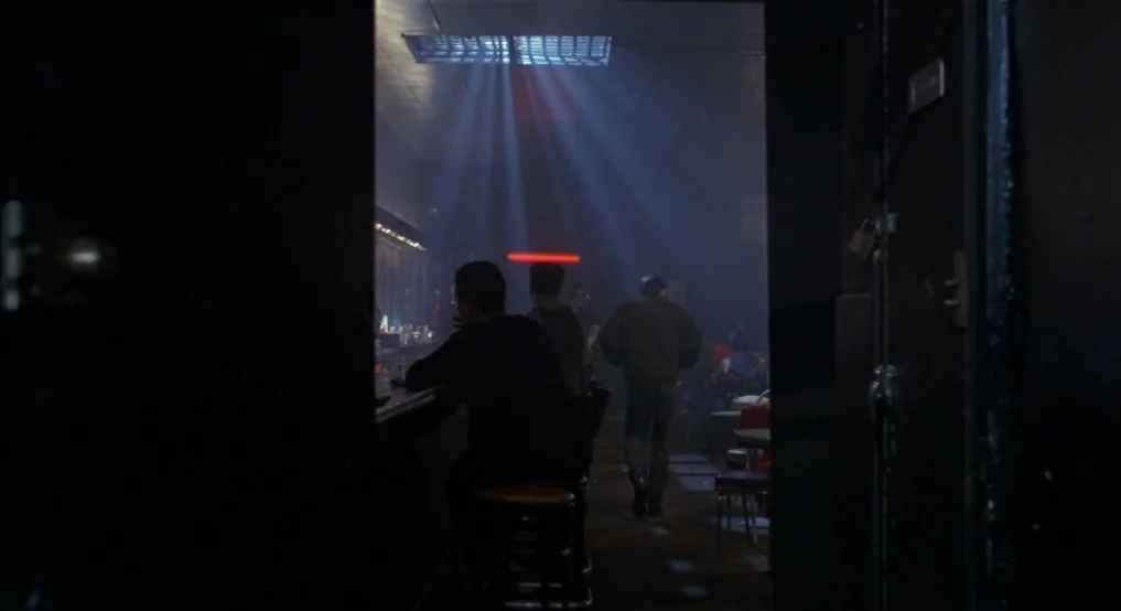 Light Sleeper (1992) movie still: wide — A dimly lit drinking establishment features silhouettes of patrons and overhead atmospheric light rays. Men…