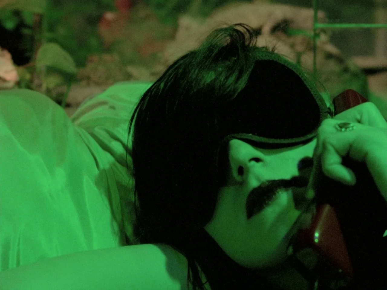 Decoder (1984) movie still: closeup — A person lies on a soft surface while wearing a sleep mask. They hold a dark red telephone receiver near their…