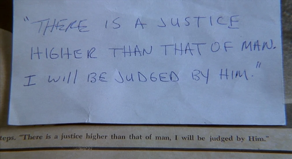 Misery (1990) movie still: closeup — A piece of wrinkled white paper with handwritten blue ink sits on a book. The paper displays the quote There is…