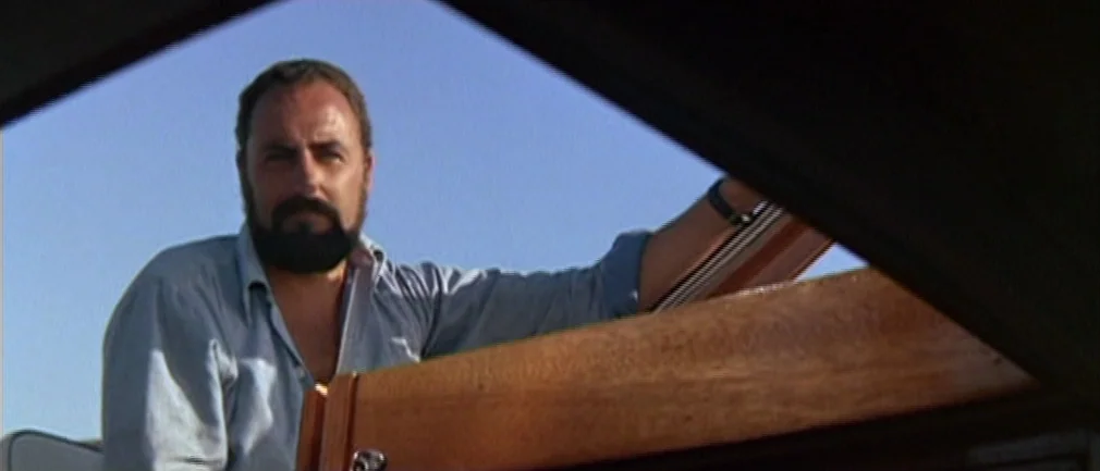 Boom! (1968) movie still: medium — A man stands on a boat under a clear blue sky. He leans against a polished wooden structure while looking toward…