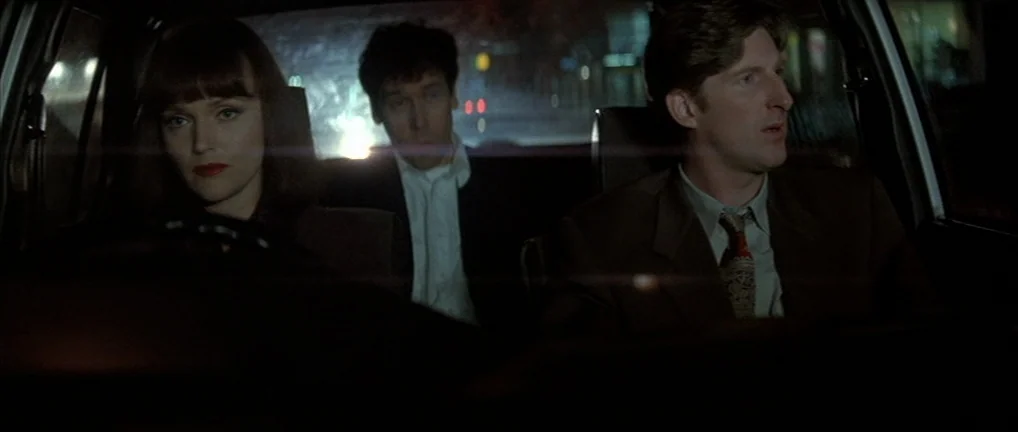 The Crying Game (1992) movie still: medium — Inside a car cabin at night, three people sit facing forward while traveling. Blurred city streetlights…