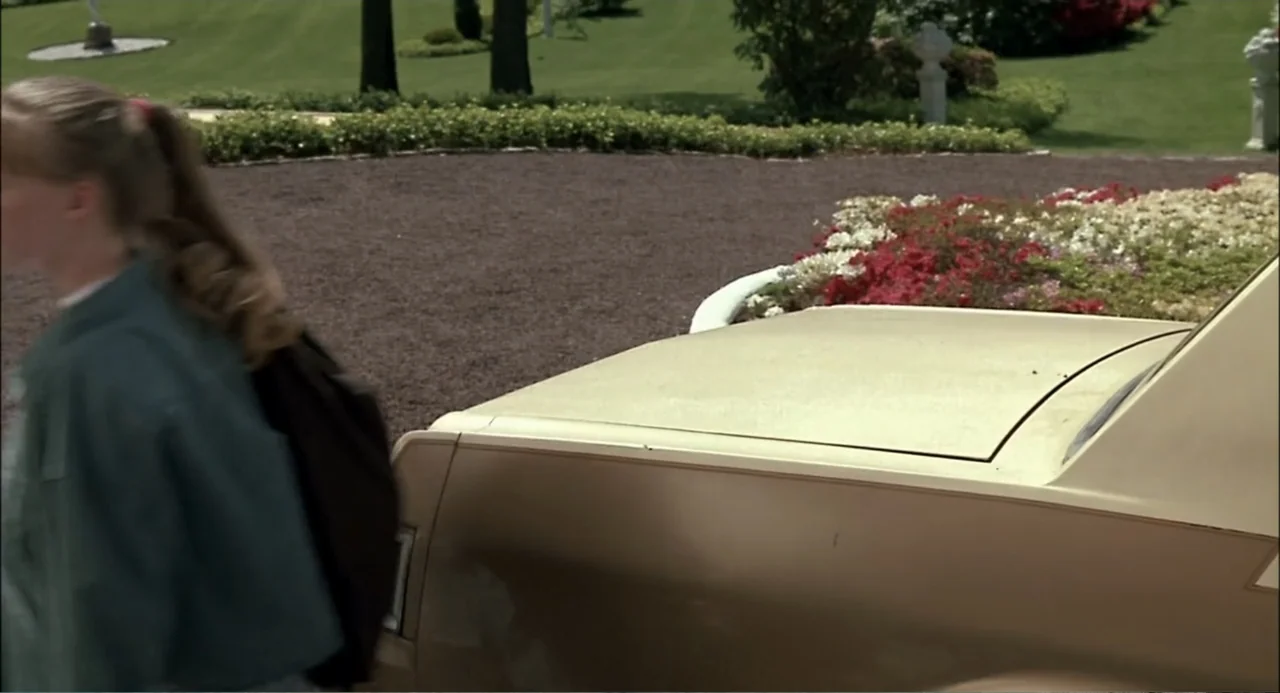 She-Devil (1989) movie still: medium — A gravel driveway borders a manicured lawn with flowerbeds and stone accents. A teenage girl with a ponytail…